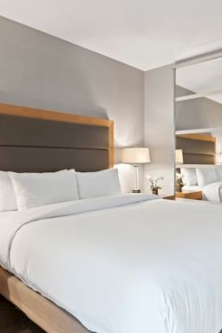 A modern hotel room with a large bed, two nightstands, table lamps, a mirrored wall, and neutral decor.