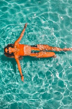 A person lounging in a turquoise ocean, floating on their back with arms and legs spread, sunlit water patterning around them.