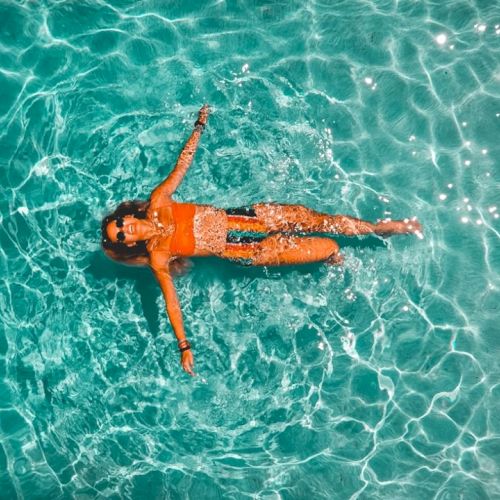 A person floating on crystal-clear turquoise water, arms and legs relaxed as sunlight creates sparkling ripples on the surface.